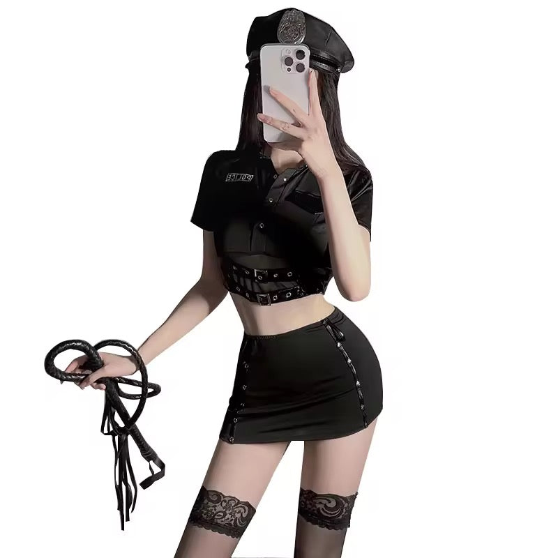 Person wearing a black outfit with a crop top and skirt, holding a phone and a whip, on a white background.