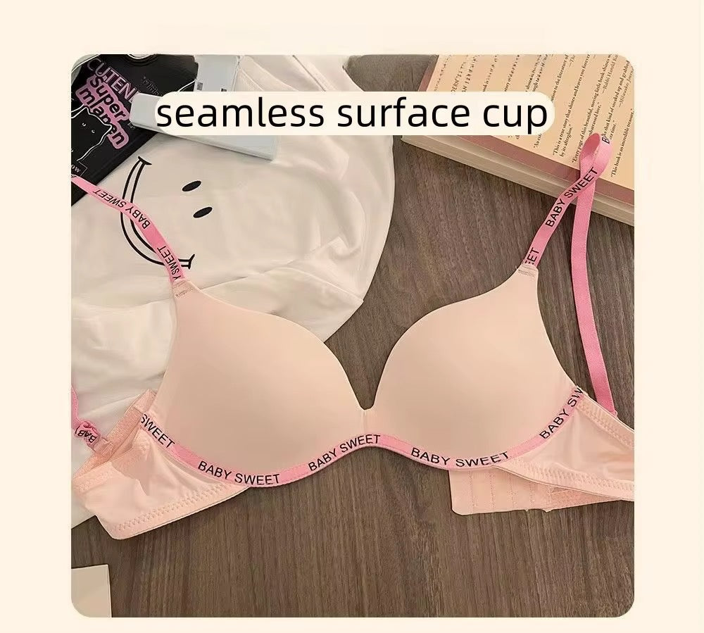 Beige bra with pink straps labeled 'Baby Sweet' on a wooden surface.