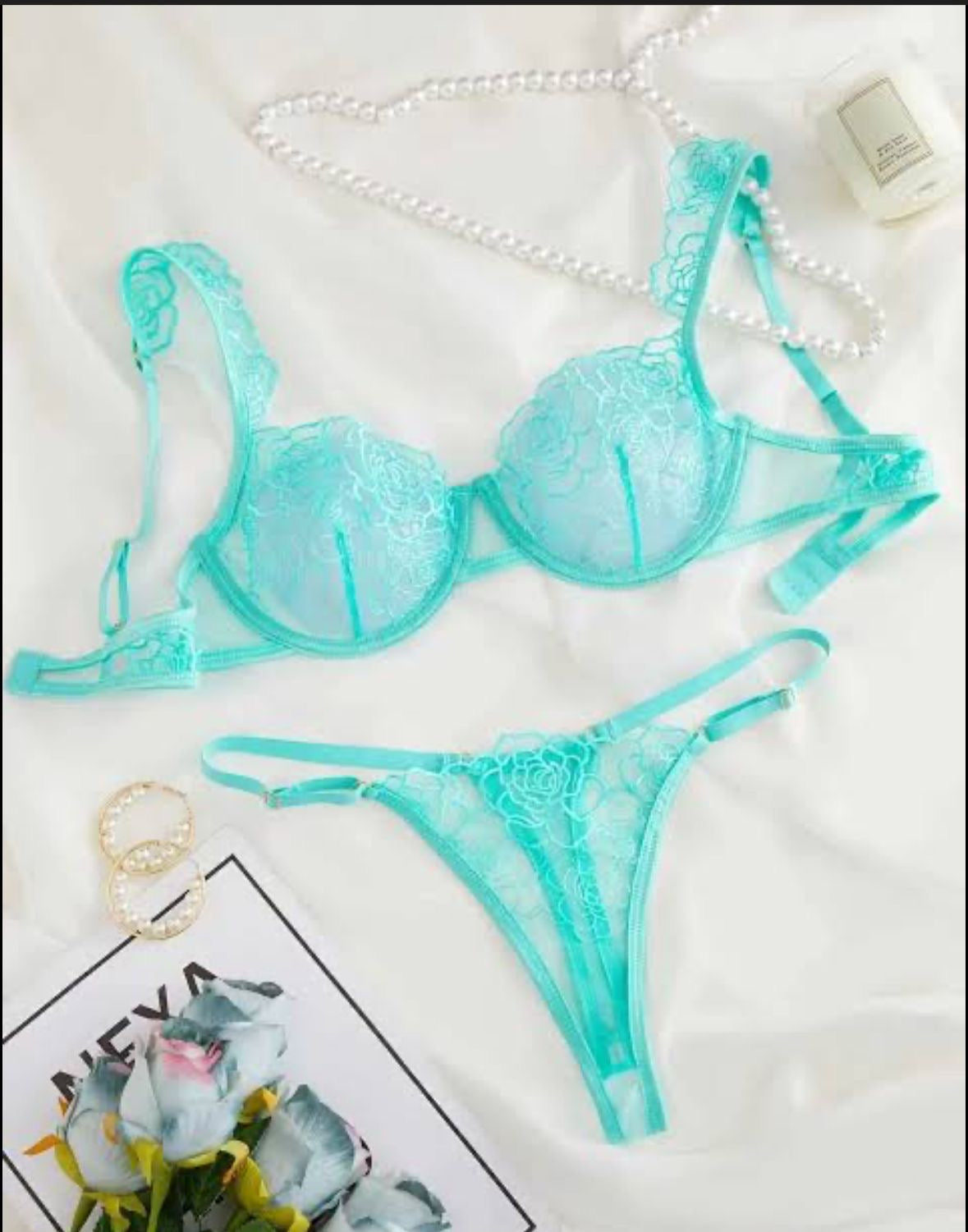 Teal lace lingerie set on a white background with a small plant and product packaging.