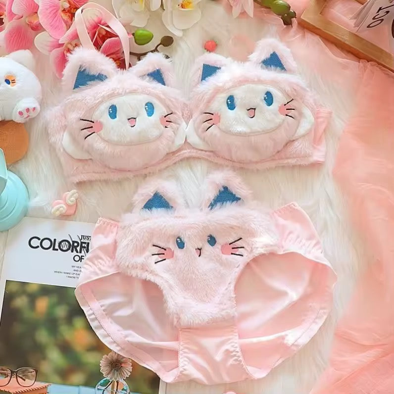 Cat-themed pink eye mask and underwear set on a soft surface with flowers and toys.
