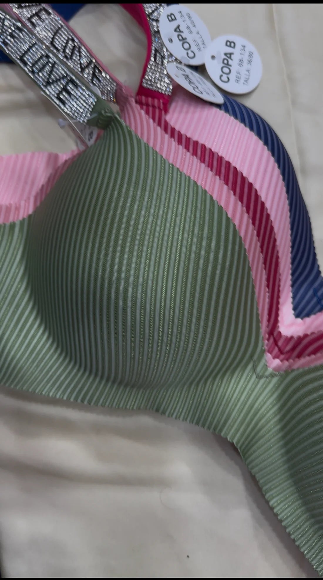 Green ribbed bra with pink and blue straps on a beige background