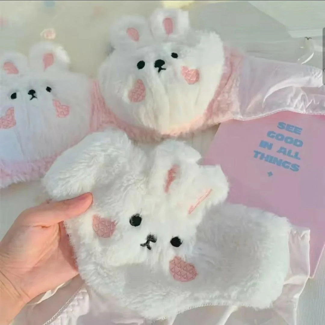 White plush toy with pink cheeks and black eyes held by a hand, with another similar toy in the background.