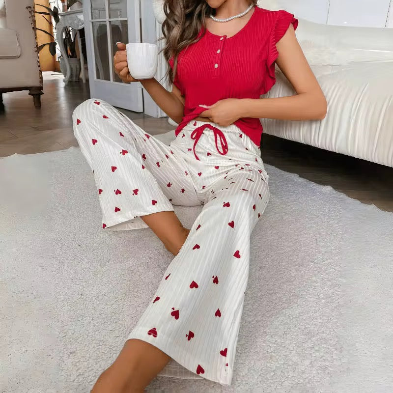Woman in red top and white pants with red heart patterns sitting on a carpeted floor.