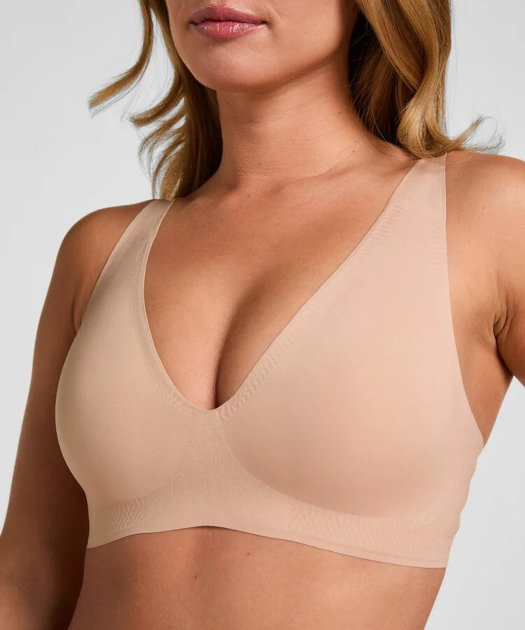 Close-up of a woman wearing a seamless, wireless bra in a light nude beige color, showing the molded cup and wide shoulder straps against a plain light gray background.