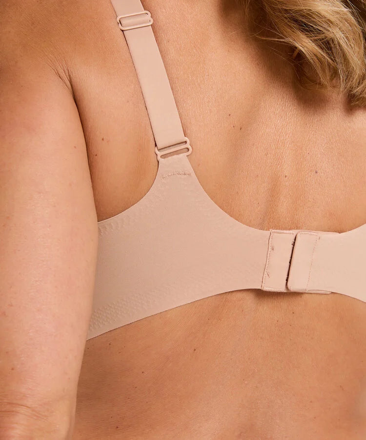 Close-up back view of a person wearing a seamless bra in a light nude beige color, showing the adjustable straps and back closure.