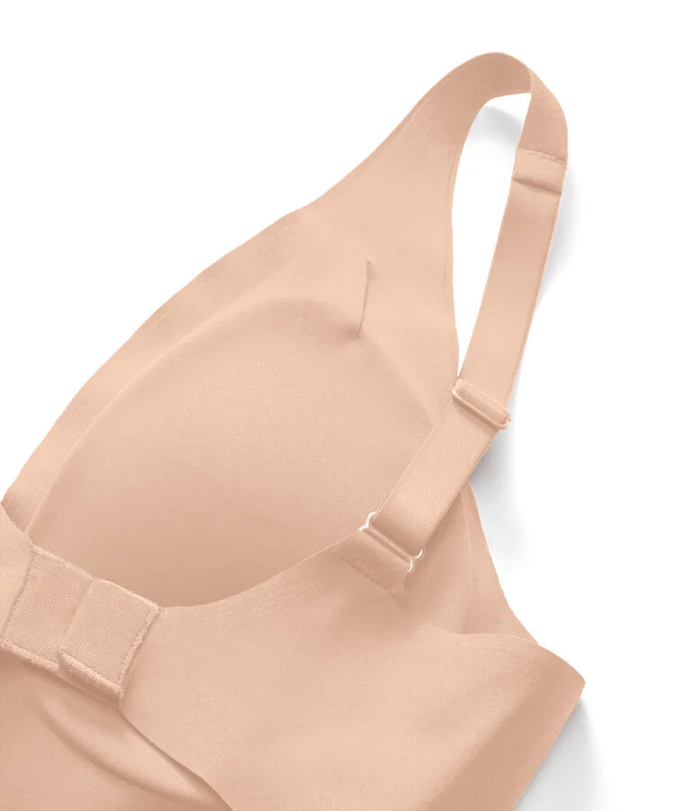 Close-up of a seamless, strapless bra in a light peach-beige color, showing the molded cup, underband, and adjustable shoulder straps on a white background.