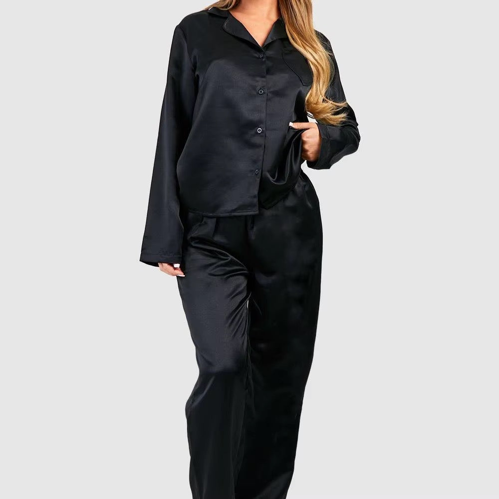 A woman wearing a black satin pajama set with a long-sleeve button-up shirt and matching pants, shown against a light gray studio background.