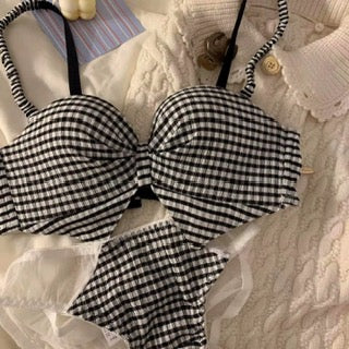 A black and white gingham bikini set with a large bow on the bra and matching ruffled bottoms, styled on a white lace top.