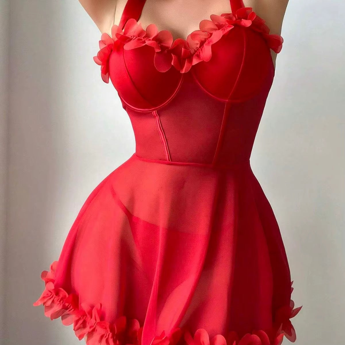 A bright red vintage-style sweetheart dress with floral ruffle details on the bust and hem, shown on a model against a neutral light gray background.