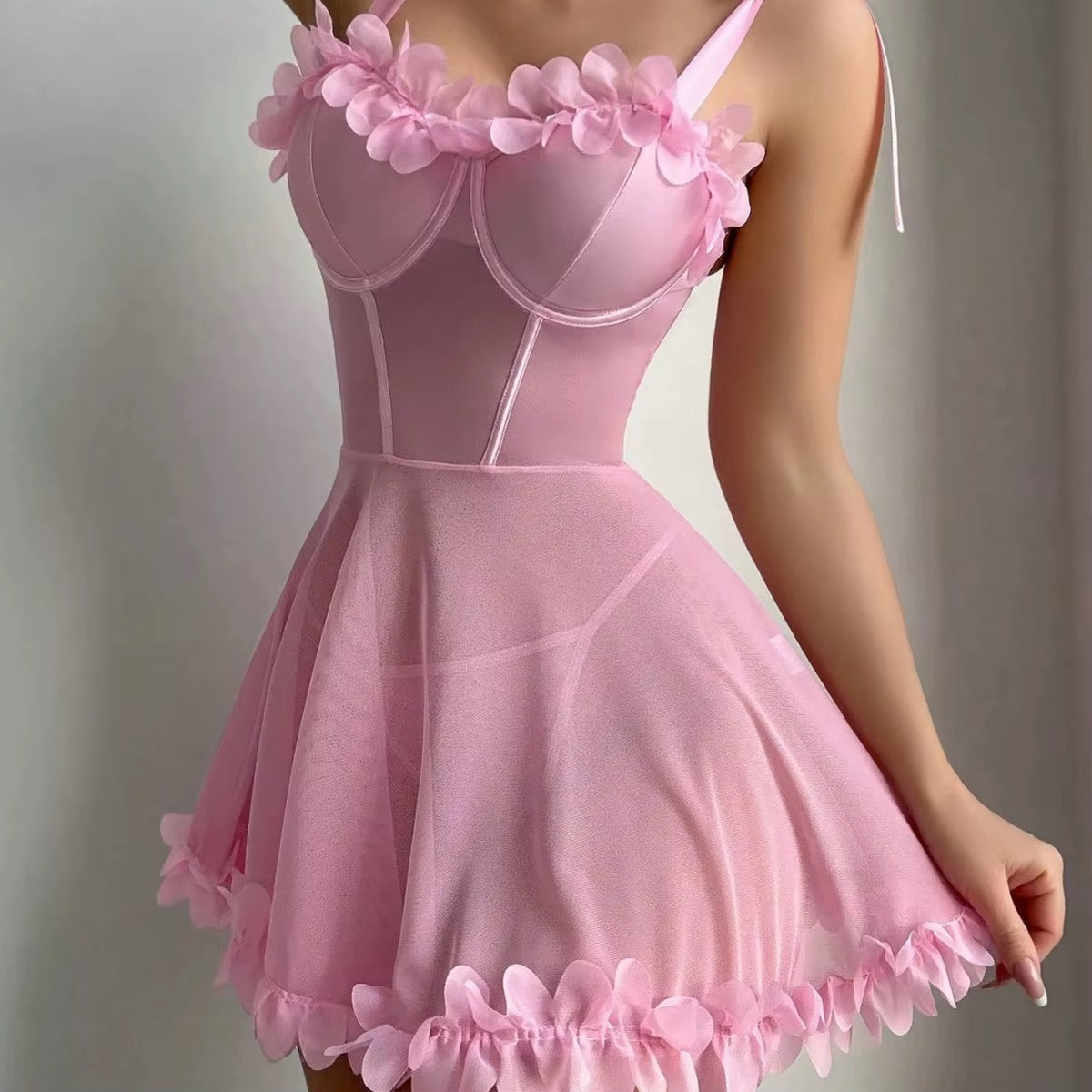 A pink corset-style mini dress with a flared skirt, floral embellishments along the neckline, and a ruffled hem, shown on a model against a neutral gray background.