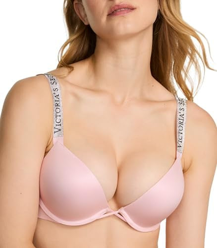 A close-up of a model wearing a light pink Victoria's Secret bra, showing the smooth fabric and the brand name printed on the white shoulder straps.
