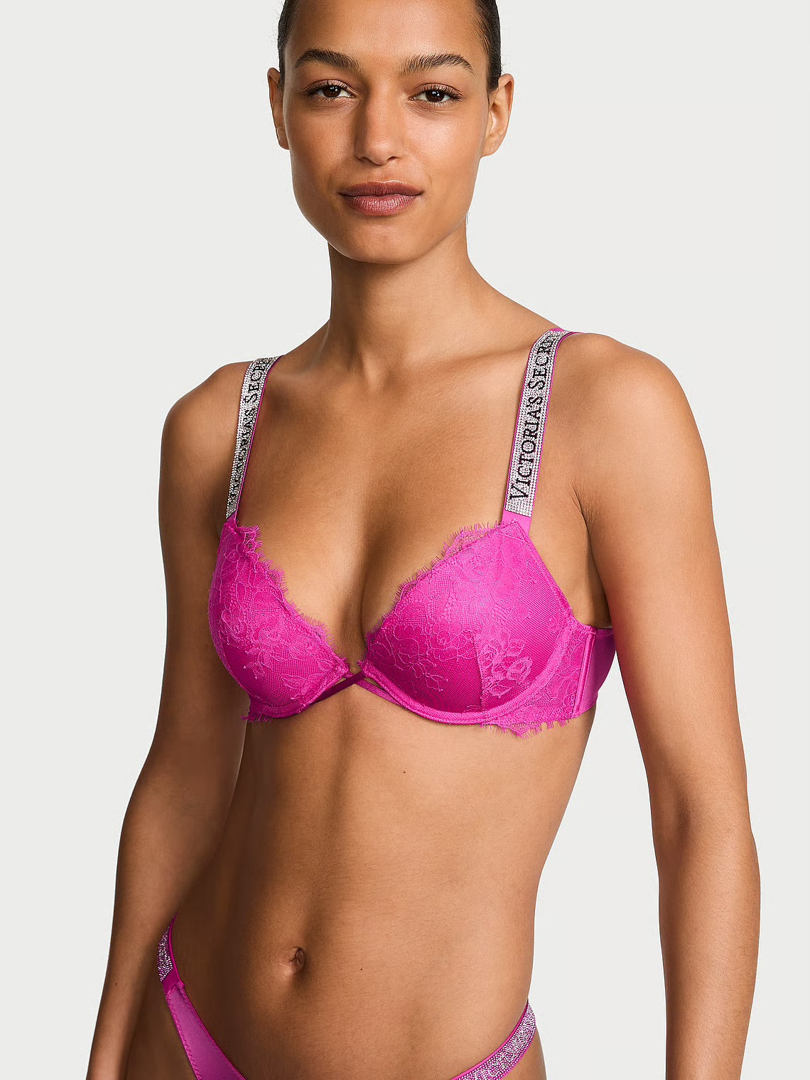 A model wearing a bright pink lace bra from Victoria's Secret, shown from the chest up against a light gray studio background.