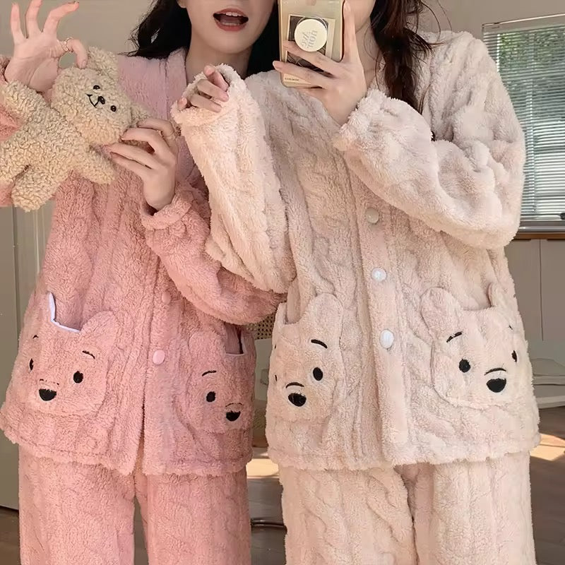 Two people wearing plush pajama sets with bear face designs, one in pink and the other in white.