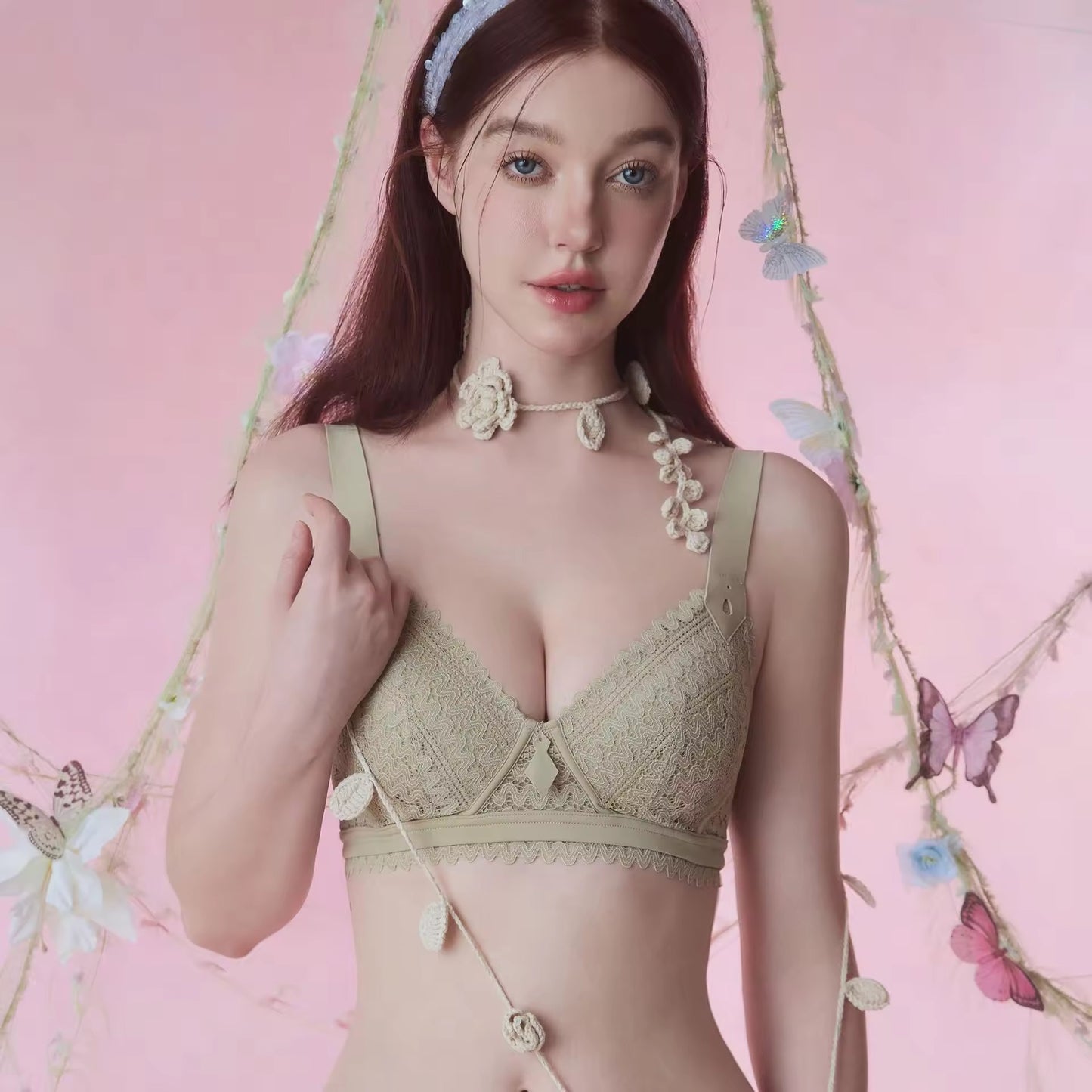 Woman wearing a green lace bralette against a pink background with floral and butterfly decorations.