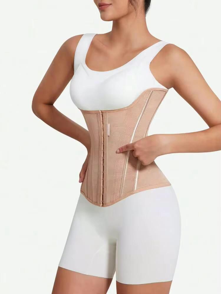 A woman wearing a beige waist trainer corset over a white sports bra and white fitted shorts, shown against a plain light background.